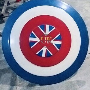 May include: A round shield with a blue outer ring, a white middle ring, and a red center. The center features a design with white and blue elements, and the letters "UK" are visible.