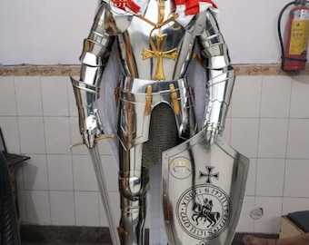 Puede incluir: Una armadura completa de acero pulido, que incluye un casco, peto y extremidades articuladas. La armadura presenta detalles dorados y un diseño de cruz roja y blanca en los hombros. También se incluye un escudo con una cruz y una espada.