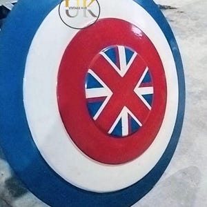 May include: A round shield with a blue, white, and red color scheme. The shield features a central red emblem with a white and blue cross design. The outer edge is blue, with a white and red ring in the center. The logo "UK VINTAGE HUB" is in the center.