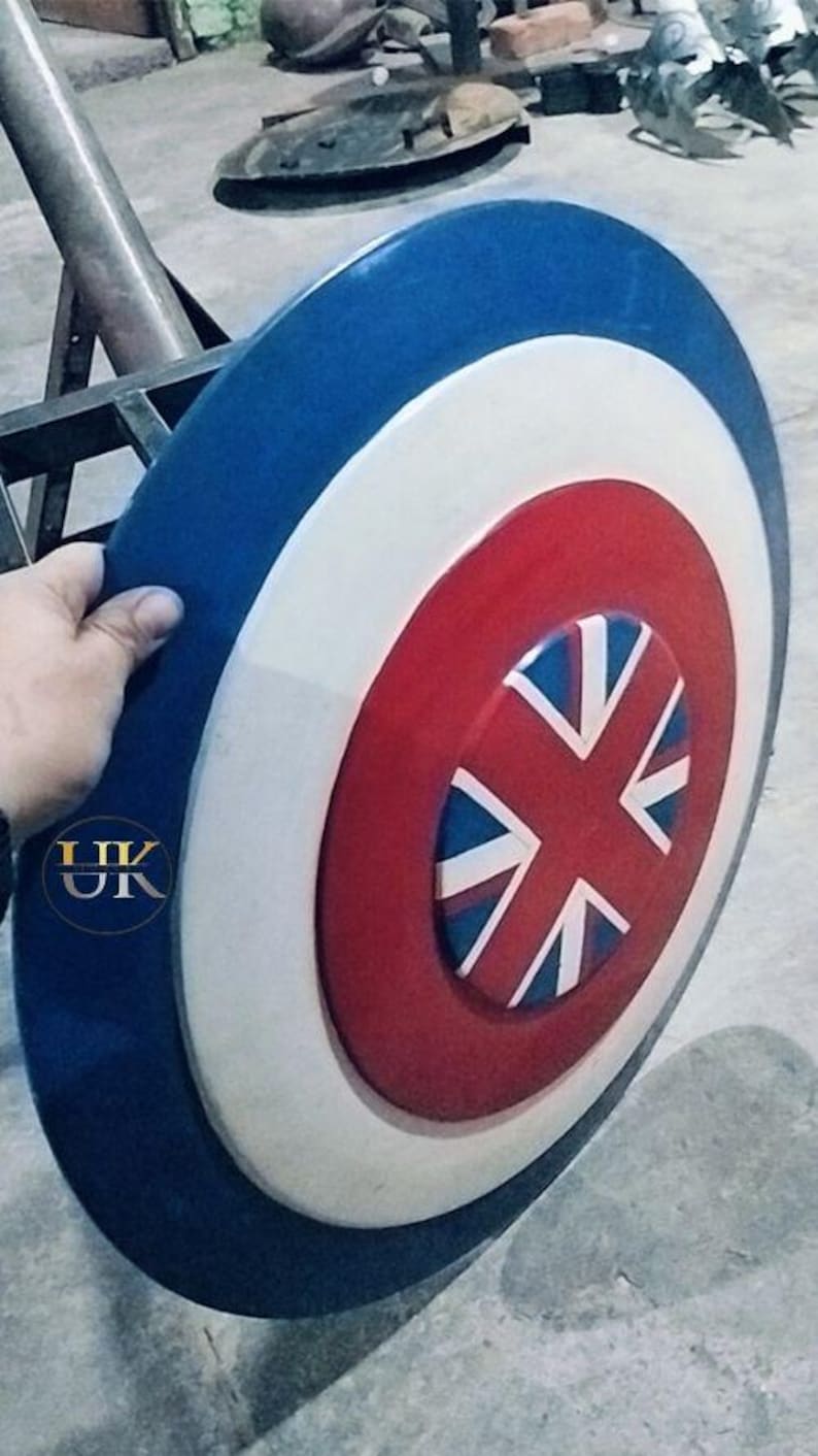 May include: A round shield with a blue outer ring, a white middle ring, and a red center. The center features a Union Jack design. The shield is held by a hand.