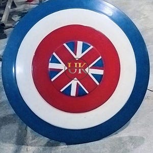 May include: A round shield with a blue outer ring, a white middle ring, and a red center. The center features a Union Jack design with the letters "UK" in the middle. The shield is likely made of metal.