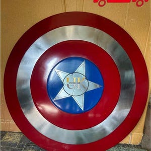 K&ouml;nnte beinhalten: Ein kreisf&ouml;rmiger Schild mit konzentrischem Design, bestehend aus einem dunkelroten Au&szlig;enring, einem metallisch silbernen Mittelring und einem blauen Innenkreis mit einem gro&szlig;en silbernen f&uuml;nfzackigen Stern. Der Text VINTAGE HUB ist aufgedruckt.