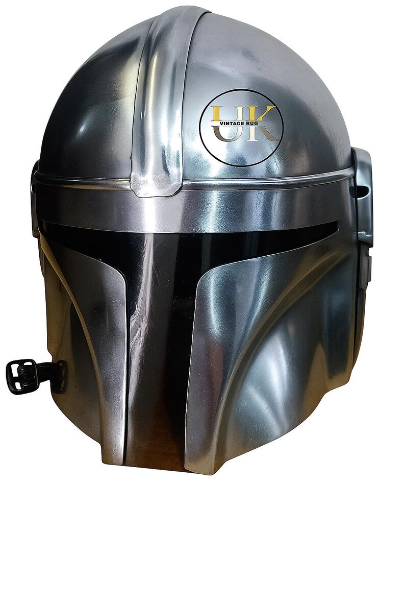 May include: A silver-colored Mandalorian helmet with a sleek, metallic finish. The helmet features a T-shaped visor and a rounded top, with a logo on the upper right side. The design is reminiscent of a space-themed character.