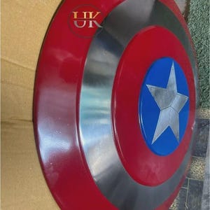 K&ouml;nnte beinhalten: Ein kreisf&ouml;rmiger Schild mit einem gl&auml;nzend roten Au&szlig;enring, einem metallisch silbernen Mittelring und einem blauen Mittelkreis mit einem markanten silbernen f&uuml;nfzackigen Stern. Der Text "UK" ist in roter Schrift oben links aufgedruckt.