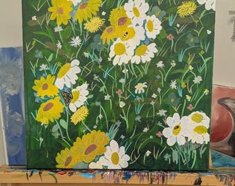 May include: An acrylic painting of a field of flowers. The canvas is filled with yellow and white daisies, with a few small blue and white flowers. The background is a dark green, and the painting is on an easel.