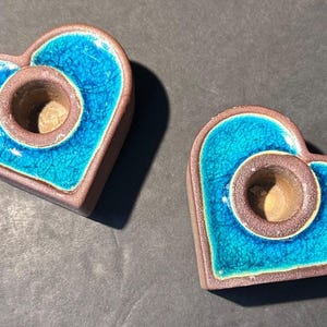 May include: Two heart-shaped candle holders. Each has a turquoise crackle glaze center and a brown rim. The center has a hole for a candle. The candle holders are made of ceramic.