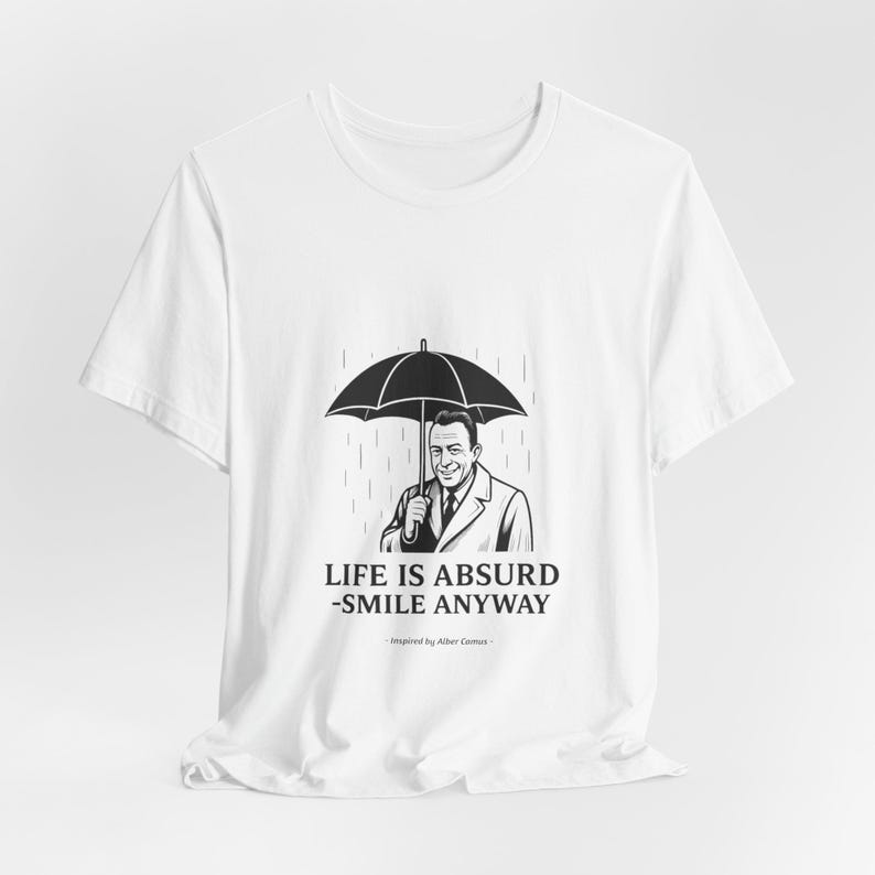 Puede incluir: Camiseta blanca con una ilustraci&oacute;n en blanco y negro de un hombre bajo un paraguas bajo la lluvia. El texto "LIFE IS ABSURD - SMILE ANYWAY" est&aacute; impreso debajo de la imagen, inspirado en Albert Camus.
