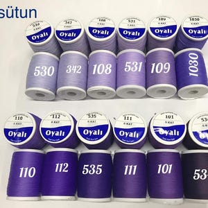 May include: An assortment of purple and lavender thread spools. Each spool is labeled with a number and the brand name "Oyalı". The spools are arranged in rows, showcasing a range of shades from light to dark.