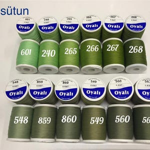 May include: A collection of green thread spools, each labeled with a unique number and the brand name "Oyali". The spools are arranged in rows, showcasing a variety of shades from light to dark green. The text "21.sütun" is at the top.