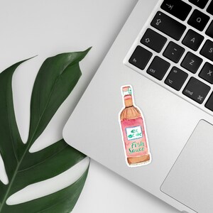 Może przedstawiać: Aquarela przedstawiająca butelkę sosu rybnego na laptopie. Butelka jest r&oacute;żowa i brązowa z białą etykietą z napisem "Sos rybny".