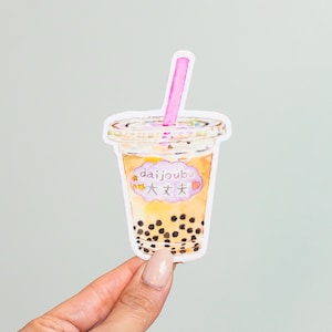 Può includere: Un'illustrazione ad acquerello di un bicchiere di bubble tea con una cannuccia rosa. Il bicchiere ha un coperchio bianco e un adesivo che dice "daijoubu 大丈夫" in giapponese. L'adesivo è rosa con un cuore e stelle.