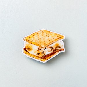 Può includere: Un'illustrazione ad acquerello di un s'more con marshmallow tostato. Lo s'more è fatto con due biscotti graham e un marshmallow tostato. Il marshmallow è appiccicoso e fuso, e i biscotti graham sono leggermente dorati.