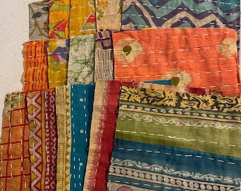 May include: A collection of colorful, patterned fabric pieces. The fabrics feature various designs, including geometric shapes, floral patterns, and stripes, in shades of orange, blue, green, and yellow. White stitching is visible throughout the pieces.