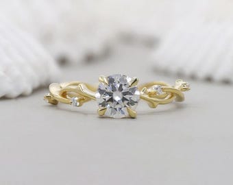Könnte beinhalten: Ein goldener Verlobungsring mit einem großen, runden, klaren Edelstein als Mittelpunkt. Das Band hat ein zartes, verschlungenes Weinreben-Design mit kleinen Akzentsteinen, wodurch eine von der Natur inspirierte Ästhetik entsteht. Der Ring ist vor einem weichen, neutralen Hintergrund platziert.