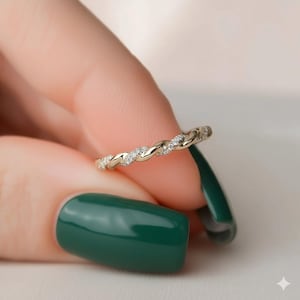 May include: A gold ring featuring a twisted band, set with small, clear gemstones. The ring is held between fingers with dark green nail polish.