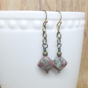 May include: A pair of dangle earrings with a square-shaped green and pink stone bead and a brass chain. The earrings have a brass hook closure.