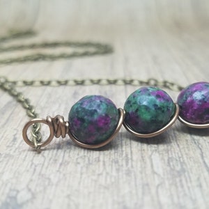 May include: A delicate necklace with a bronze chain and three green and pink gemstone beads wrapped in copper wire.