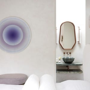 Puede incluir: Dise&ntilde;o interior minimalista con una obra de arte mural circular en tonos morados y azules. Se observa un ba&ntilde;o moderno con espejo con marco de cobre, lavabo de m&aacute;rmol y apliques de pared decorativos.