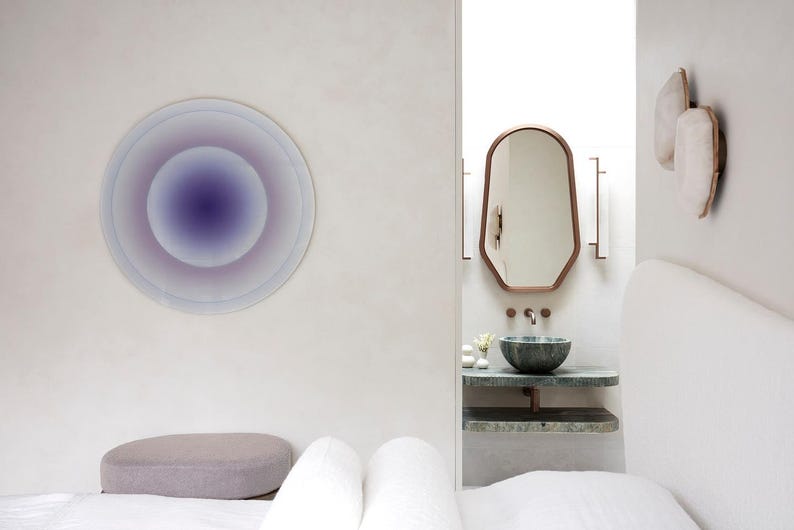 Puede incluir: Dise&ntilde;o interior minimalista con una obra de arte mural circular en tonos morados y azules. Se observa un ba&ntilde;o moderno con espejo con marco de cobre, lavabo de m&aacute;rmol y apliques de pared decorativos.