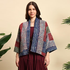 Könnte beinhalten: Eine Patchwork-Jacke mit verschiedenen Mustern und Farben, darunter Rot, Blau und Grün. Die Jacke hat einen Schalkragen und Taschen. Das Kleidungsstück wird über einem bordeauxfarbenen Kleid getragen.