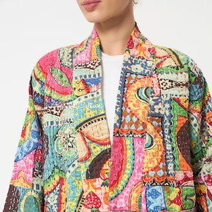 Pu&ograve; includere: Una giacca trapuntata caratterizzata da un vivace patchwork di motivi multicolori che includono rosa, verde, giallo e blu. Il capo presenta un colletto a scialle, maniche lunghe e dettagli visibili di impunture bianche sul tessuto.