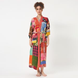 Puede incluir: Una bata de manga larga con un diseño de patchwork que presenta varios patrones coloridos en rojo, naranja, azul, verde y negro. La prenda tiene un cierre de lazo en la cintura, dos bolsillos delanteros y el texto Kantha Culture impreso.