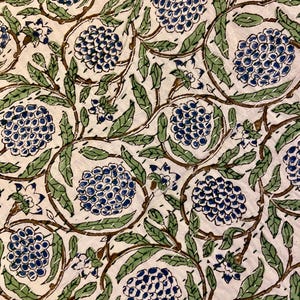 May include: A close-up of a white fabric with a repeating floral pattern. The design features blue, green, and brown elements, including stylized flowers and leaves. The fabric is stitched with white thread, creating a quilted effect.