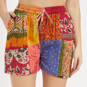 Puede incluir: Shorts de patchwork multicolores con cintura elástica y cordón. Los shorts están hechos de varias telas estampadas en tonos rojos, naranjas, amarillos, verdes y azules.