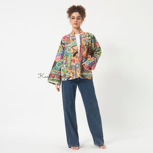 Pu&ograve; includere: Una giacca a maniche lunghe aperta sul davanti con un vivace motivo patchwork multicolore caratterizzato da intricati disegni floreali e geometrici. La giacca &egrave; indossata sopra un top bianco semplice e jeans blu scuro. Il testo Kantha Couture &egrave; visibile.