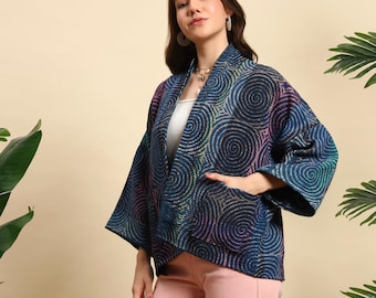 Può includere: Giacca stile kimono blu scuro con un motivo a spirale nei toni del blu, verde e rosa. La giacca ha maniche larghe e tasche. La modella indossa un top bianco e pantaloni rosa.