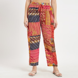 Op de afbeelding: Patchworkbroek in roze, rode en blauwe tinten. De broek heeft een tailleband met trekkoord en een patchworkontwerp met verschillende patronen en texturen. De broek is gemaakt van een zachte, lichte stof.