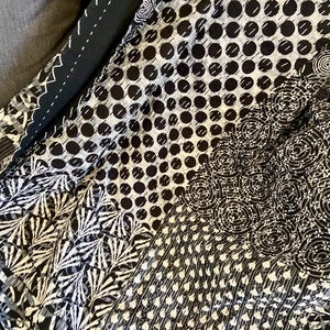 May include: A patchwork textile featuring a variety of black and white patterns. The designs include polka dots, floral motifs, and geometric shapes. The fabric is folded, revealing different sections of the design.