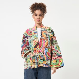 May include: A long-sleeved, open-front jacket featuring a vibrant, multicoloured patchwork pattern with intricate stitching. The garment displays a variety of geometric and organic shapes in shades of pink, yellow, blue, and green, worn over a white shirt.