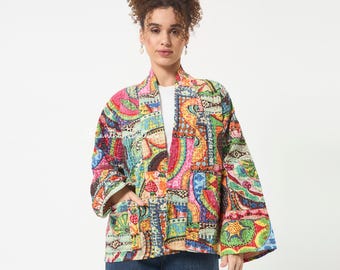 Puede incluir: Una chaqueta de manga larga abierta por delante con un vibrante patrón de patchwork multicolor y costuras intrincadas. La prenda muestra una variedad de formas geométricas y orgánicas en tonos rosa, amarillo, azul y verde, sobre una camiseta blanca.