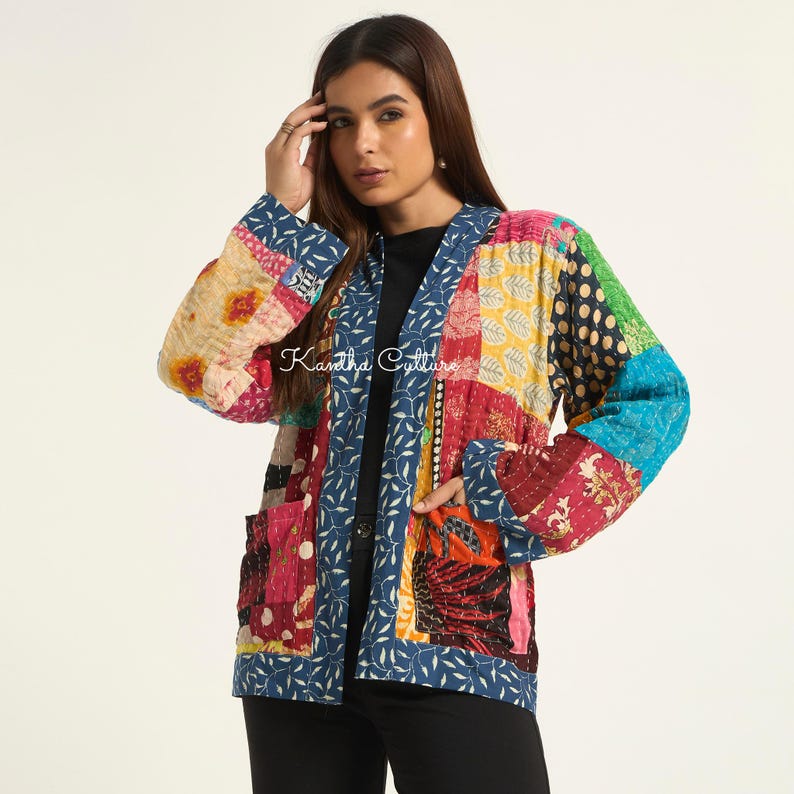 Puede incluir: Una chaqueta de manga larga con un dise&ntilde;o de retazos de varias telas coloridas con costuras intrincadas. La prenda tiene un borde azul con un patr&oacute;n de hojas blancas a lo largo de la abertura frontal y dos bolsillos. El texto Kantha Culture es visible.