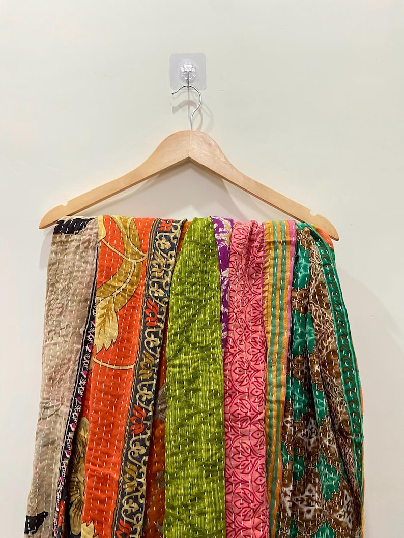 May include: A colorful, patchwork textile hanging on a wooden hanger. The textile features a variety of patterns and colors, including orange, green, pink, and brown. The fabric appears to be stitched together with visible seams.