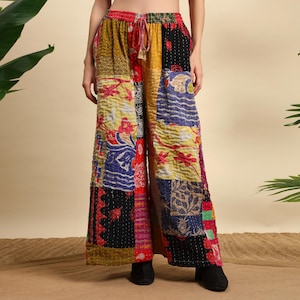Puede incluir: Pantalones palazzo patchwork con cintura con cordón. Los pantalones de pernera ancha presentan una variedad de parches de tela coloridos en amarillo, rojo, azul y negro. El diseño patchwork incluye patrones florales y geométricos. Los pantalones se llevan con zapatos negros.