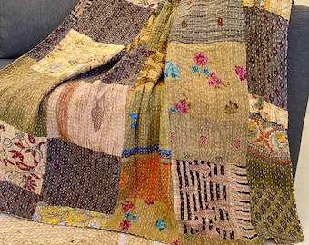 Puede incluir: Una colcha de retazos multicolor drapeada sobre un sofá gris. La colcha está hecha de varias telas en tonos de marrón, naranja, rojo y verde. El diseño está formado por múltiples cuadrados cosidos, creando una textura única.