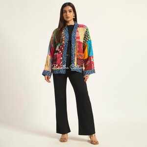 Puede incluir: Una chaqueta de manga larga con un dise&ntilde;o de patchwork que presenta varios patrones y texturas coloridas. La chaqueta tiene un borde azul con un estampado de hojas blancas a lo largo de la abertura frontal y los pu&ntilde;os. El texto Kantha Culture es visible.