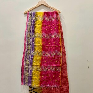 May include: A colorful textile hanging on a wooden hanger. The textile features vertical stripes of purple, yellow, and pink, with intricate embroidered patterns and a red border. The fabric appears to be made of a soft material.