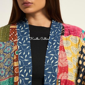 Puede incluir: Una chaqueta acolchada con un dise&ntilde;o de patchwork que presenta varios patrones coloridos, incluyendo motivos florales, de hojas y de lunares. La prenda tiene un cuello azul con un estampado de hojas blancas y el texto Kantha Culture en blanco.