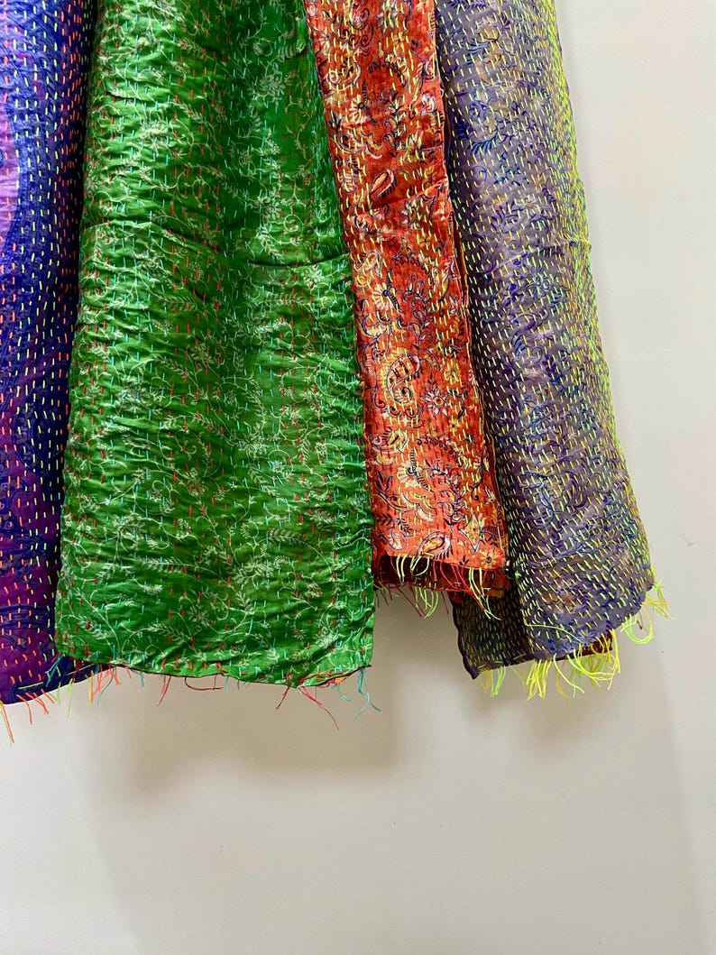 Op de afbeelding: Close-up van kleurrijke, getextureerde stoffen panelen. De panelen zijn in tinten paars, groen, rood en blauw. Elk paneel heeft een uniek patroon en is gestikt met contrasterend garen, waardoor een patchwork-effect ontstaat. De randen hebben losse draden.
