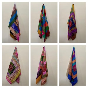 May include: A collection of six colorful patchwork scarves hanging against a neutral wall. Each scarf features a unique combination of vibrant colors and patterns, including squares, stripes, and floral designs. The scarves are made of a soft, flowing fabric.