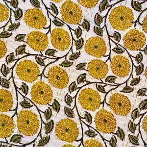 May include: A white textile with a repeating pattern of large yellow flowers and green leaves on dark brown stems. The design is hand-stitched with white thread, creating a quilted effect. The floral pattern is evenly spaced across the fabric.
