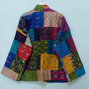 May include: A patchwork jacket with a vibrant mix of colors and patterns. The jacket features a variety of fabric squares in shades of blue, red, green, yellow, and purple. The jacket is hanging on a white wall.