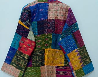 Può includere: Giacca patchwork con un vivace mix di colori e motivi. La giacca presenta quadrati di tessuto in tonalità di blu, rosso, verde, giallo e viola. La giacca è appesa a una parete bianca.