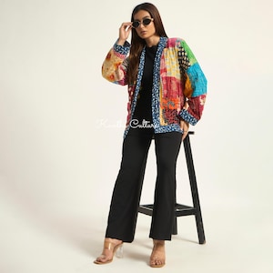 Puede incluir: Una chaqueta de patchwork de manga larga con una vibrante mezcla de cuadrados de tela multicolores en tonos rojo, azul, verde y amarillo. La chaqueta tiene un borde azul con un patr&oacute;n de hojas blancas y el texto Kantha Culture impreso en blanco.