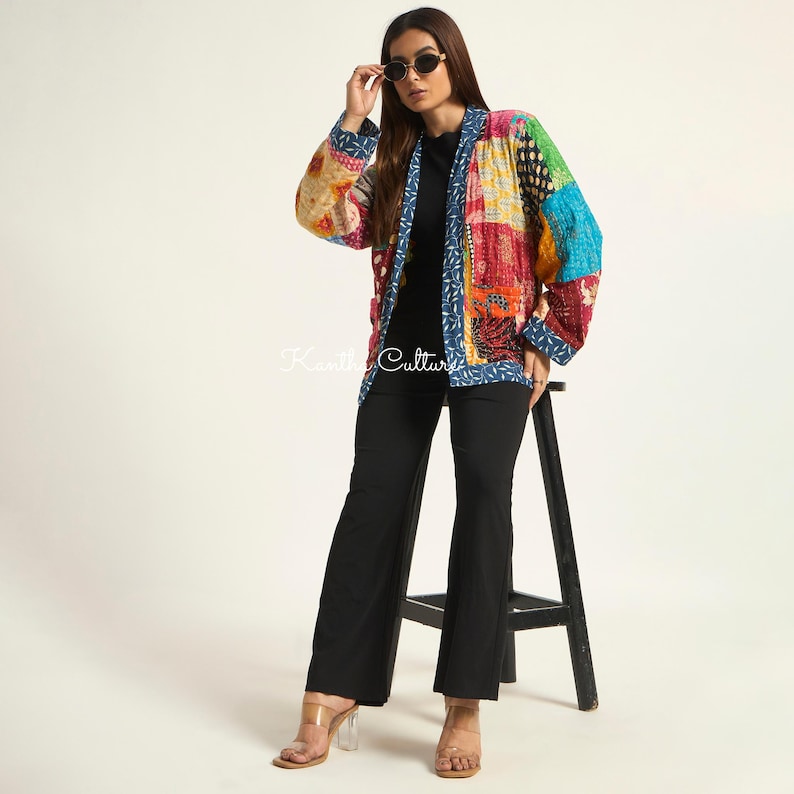 Puede incluir: Una chaqueta de patchwork de manga larga con una vibrante mezcla de cuadrados de tela multicolores en tonos rojo, azul, verde y amarillo. La chaqueta tiene un borde azul con un patr&oacute;n de hojas blancas y el texto Kantha Culture impreso en blanco.