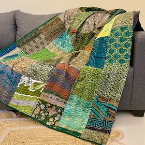 May include: A patchwork quilt in shades of green, blue, and brown, draped over a grey sofa. The quilt features a green border and is made from various patterned fabrics. The quilt is a decorative home textile.