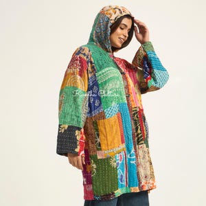 Puede incluir: Una chaqueta con capucha que presenta un diseño de patchwork de varios tejidos coloridos con patrones intrincados en tonos verde, amarillo, rojo y azul. La prenda incluye costuras visibles, mangas largas y el texto Kantha Culture en el cierre.